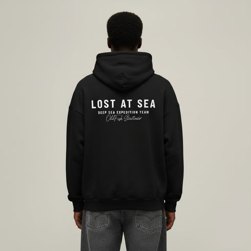 Person wearing a black hoodie with 'Lost at Sea' text on the back against a beige background