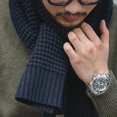 Man wearing a dark blue knitted scarf and a watch, with a blurred background