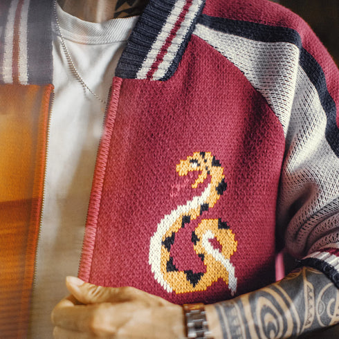 Person wearing a red knitted bag with a dragon design, held by a tattooed arm.