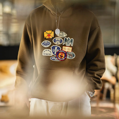 Brown hoodie with various patches worn by a person in an indoor setting