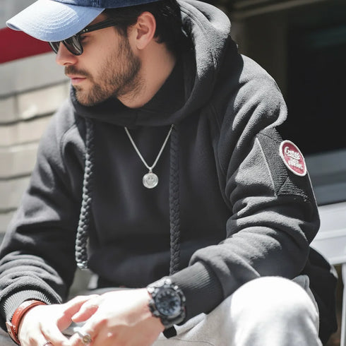 Man wearing a dark hoodie with a brand logo, sitting outdoors.