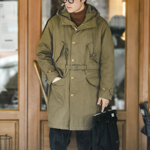Man wearing a green coat standing in front of a wooden door.