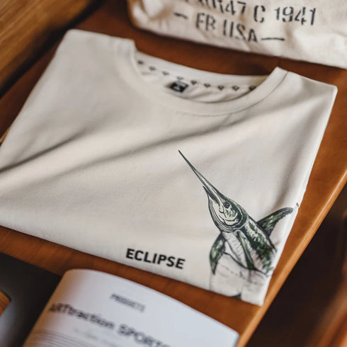 Folded white sweatshirt with a green bird graphic and 'Eclipse' text on a wooden surface.