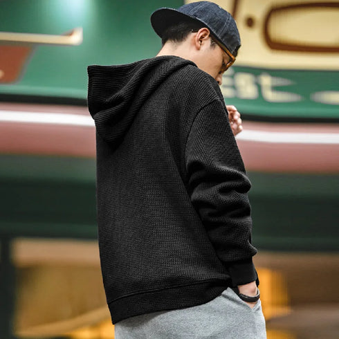 Person wearing a black hoodie and gray pants with a blurred background