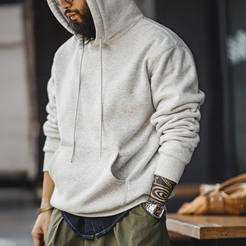 Person wearing a gray hoodie with tattoos on sleeves, standing indoors.