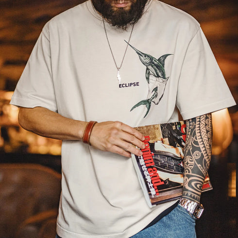 Person wearing a white t-shirt with a graphic design, holding a magazine.