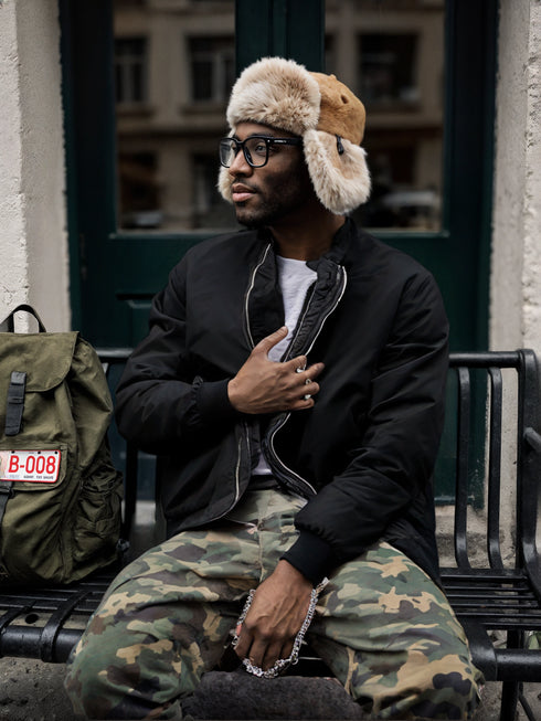 Man wearing thick embroidered black baseball winter jacket with full zipper and ribbed cuffs sitting on bench