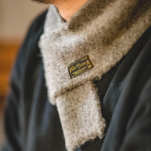 Close-up of a textured scarf with a brand label, worn by a person.