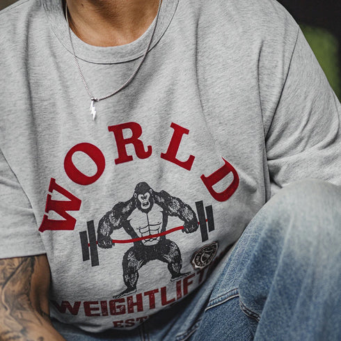 Person wearing a gray t-shirt with a graphic design of a weightlifter and 'World Weightlifter' text.