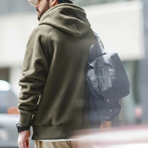 Person wearing a green hoodie and carrying a black backpack outdoors