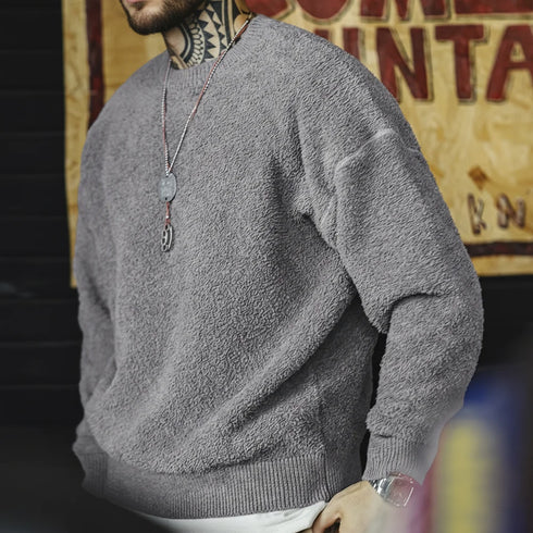 Person wearing a gray sweater with a tattooed neck against a blurred background