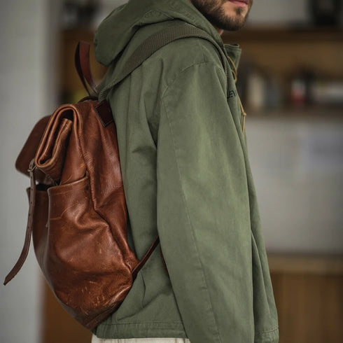 Person wearing a green jacket with a brown leather backpack