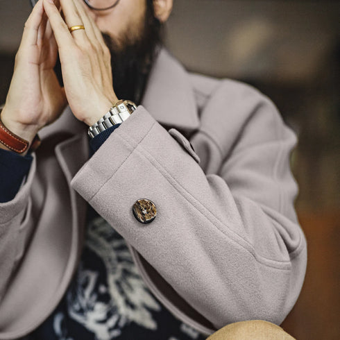 Close-up of a person wearing a beige coat with a button, blurred background
