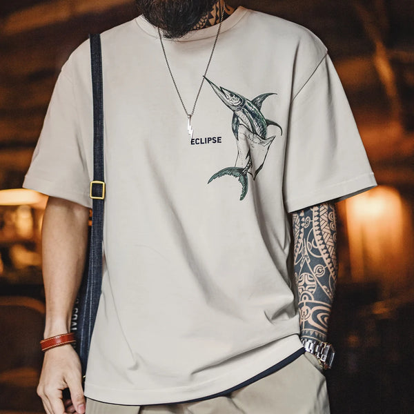 Person wearing a beige t-shirt with a fish graphic and 'Eclipse' branding, standing in a warm-lit indoor setting.