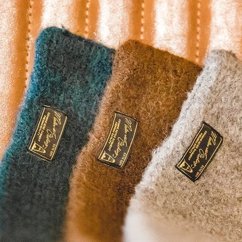 Three scarves in blue, brown, and gray with brand labels on a textured background.