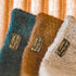 Three scarves in blue, brown, and gray with brand labels on a textured background.