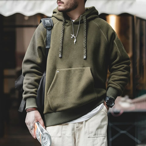 Person wearing a green hoodie with a backpack and holding a drink, blurred background