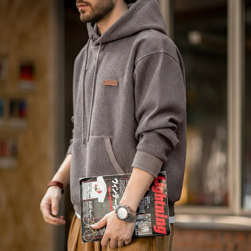 Man wearing vintage gray pullover hoodie with kangaroo pocket and adjustable hood holding magazine