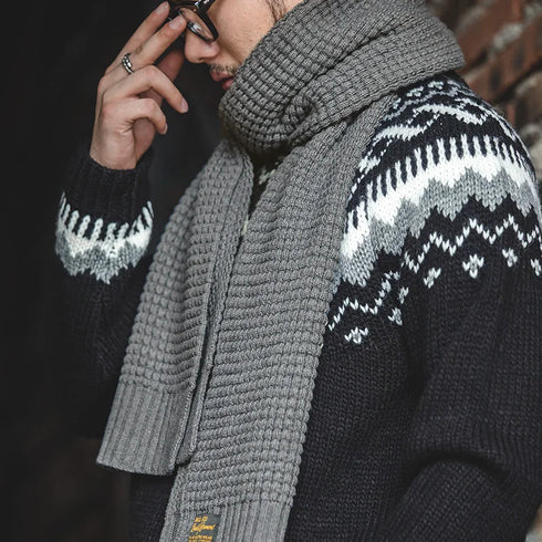 Person wearing a dark sweater with white patterns and a gray scarf.