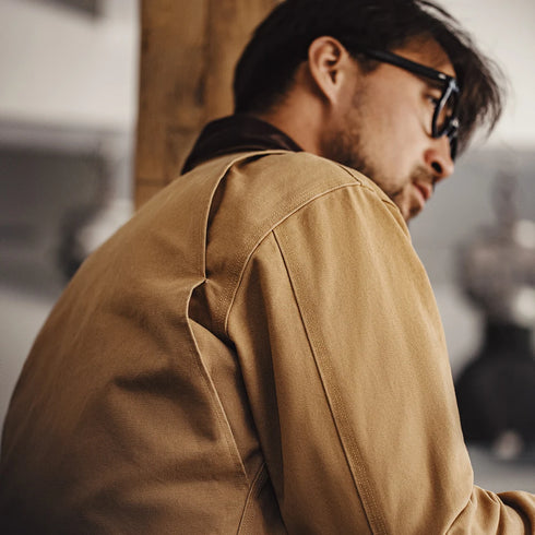 Man wearing a brown jacket and sunglasses in an indoor setting
