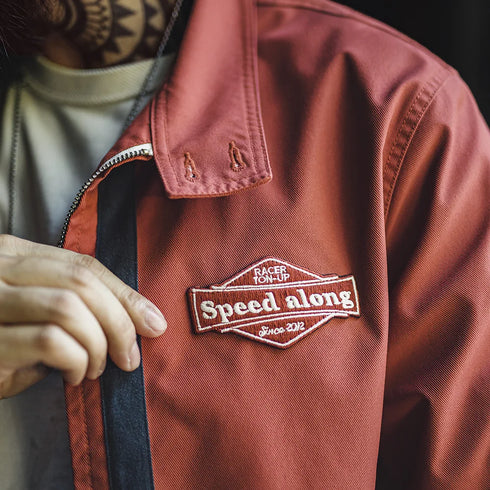 Red jacket with 'Speed along' patch on a dark background
