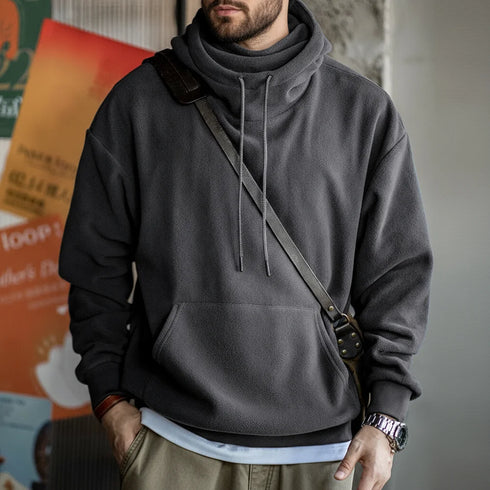 Person wearing a gray hoodie with a shoulder bag against a blurred background