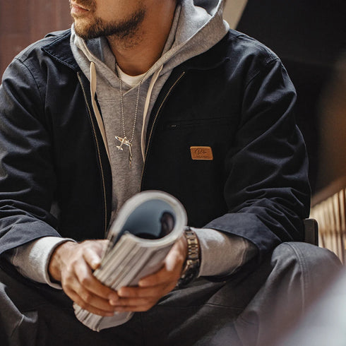 Person wearing a dark jacket and gray hoodie holding a book, with a blurred background
