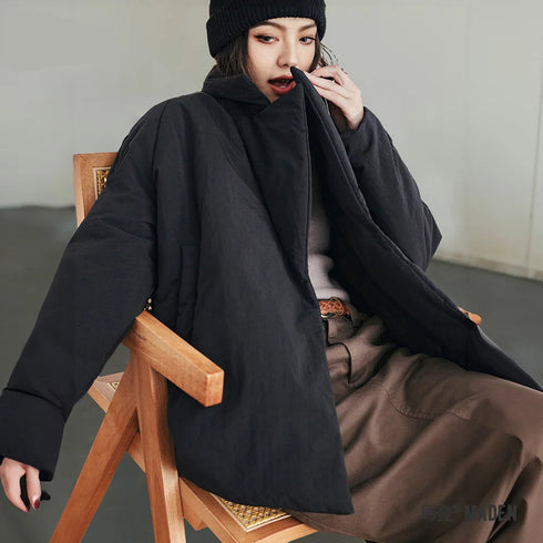 Person wearing a black coat and brown pants sitting on a wooden chair, with 'MADEN CLOTHING' branding.