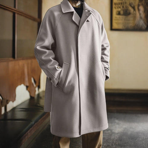 Person wearing a gray coat in an indoor setting with a vintage poster on the wall.