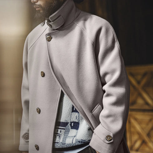 Person wearing a light gray coat with a patterned interior, standing indoors.