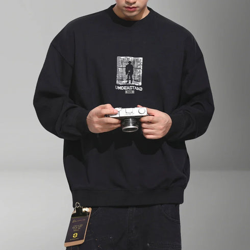 Black Japanese streetwear sweatshirt with graphic print and relaxed fit worn by man holding camera