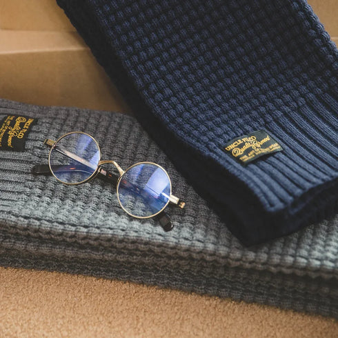 Two knit hats with labels and a pair of round glasses on a textured surface.