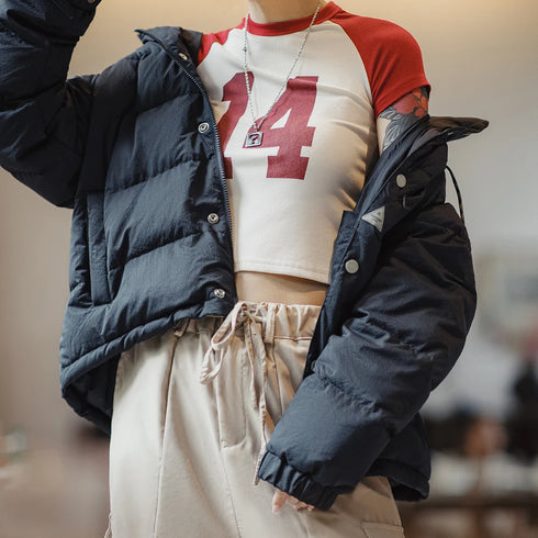 Person wearing a navy puffer jacket over a red and white sports jersey with beige pants.