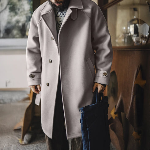 Person wearing a long coat holding a jacket indoors.