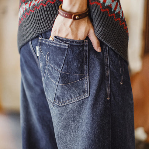 Person wearing blue jeans with a patterned sweater and leather strap.