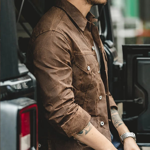 Person wearing a brown jacket leaning against a vehicle