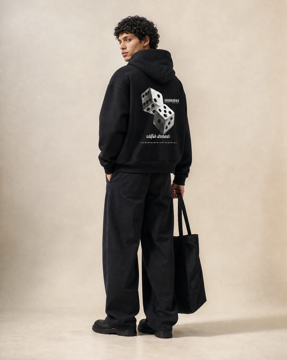 Model wearing the OddFish Double Down 500 GSM heavyweight black hoodie, shown from the back with a large double dice graphic, paired with relaxed black jeans and a black tote bag.