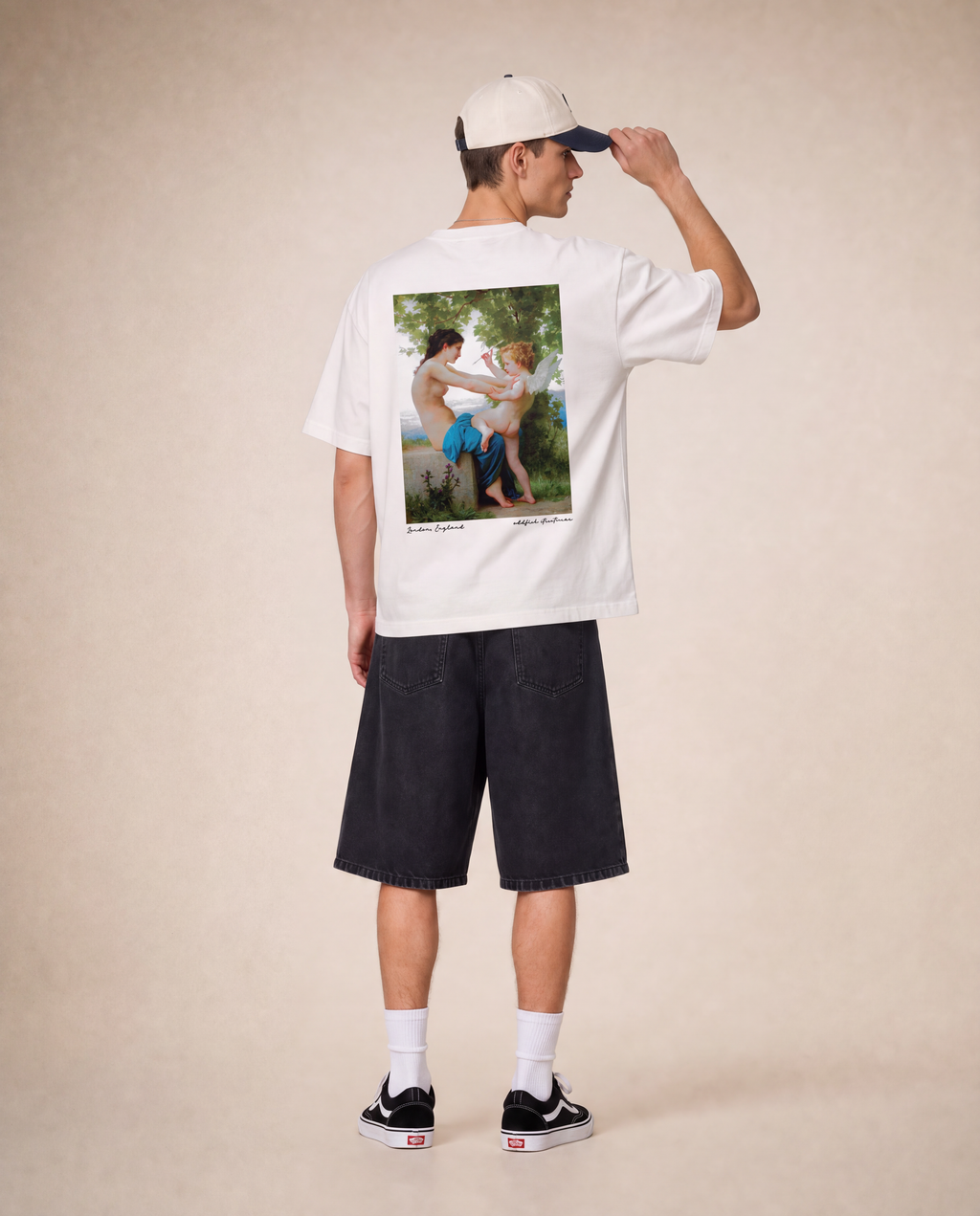 A model shown from the back wearing a white t-shirt with a large vintage-style photographic print on the back, paired with dark denim shorts, a cream baseball cap, white socks, and black sneakers, set against a warm beige studio backdrop.
