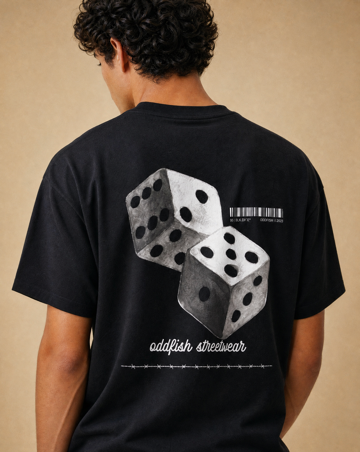 A man wearing a black t-shirt, viewed from the back. The shirt features a graphic print of two gray 3D dice, a barcode, and the text 'oddfish streetwear' in white.