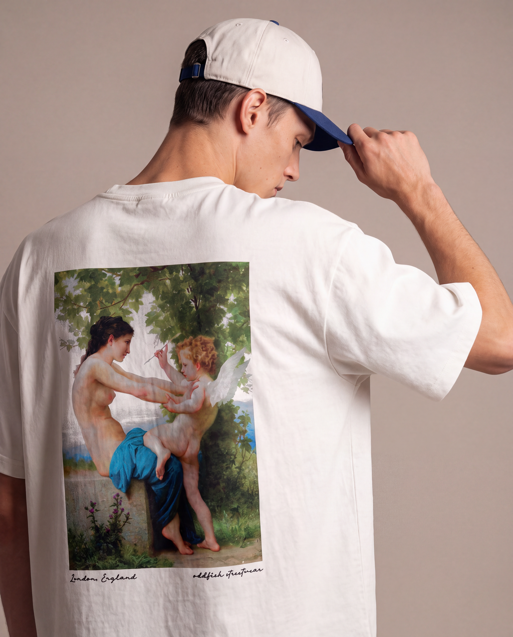 A man wearing a white t-shirt with a large classical painting print on the back, shown from behind. He is also wearing a white baseball cap with a blue visor, set against a plain beige studio background.